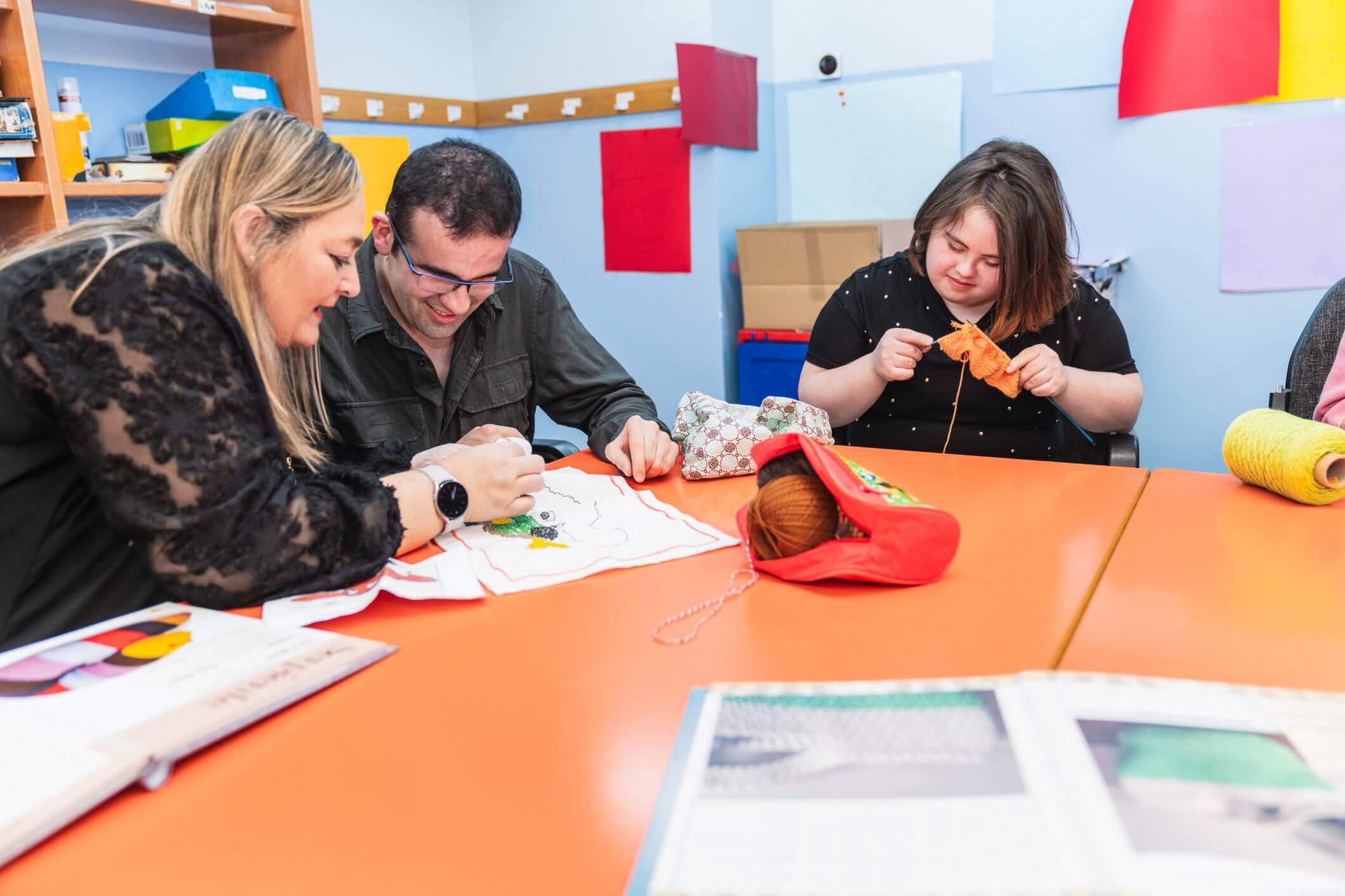 Three adults concentrating on crafts at a table in a classroom.