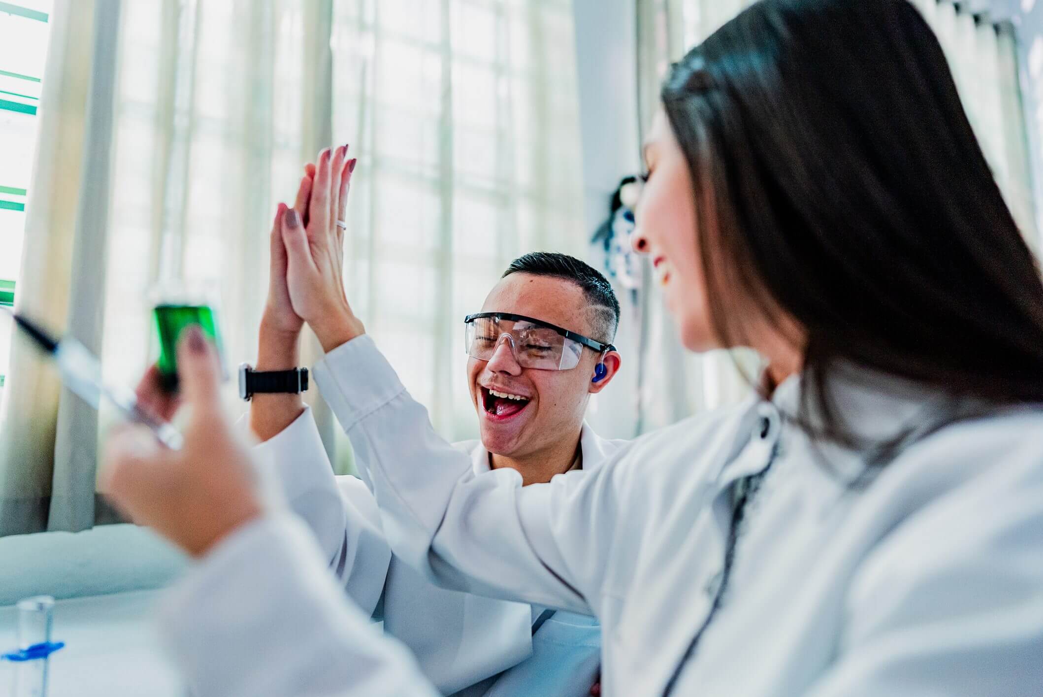 Two scientists celebrating a success with a high five in the lab.
