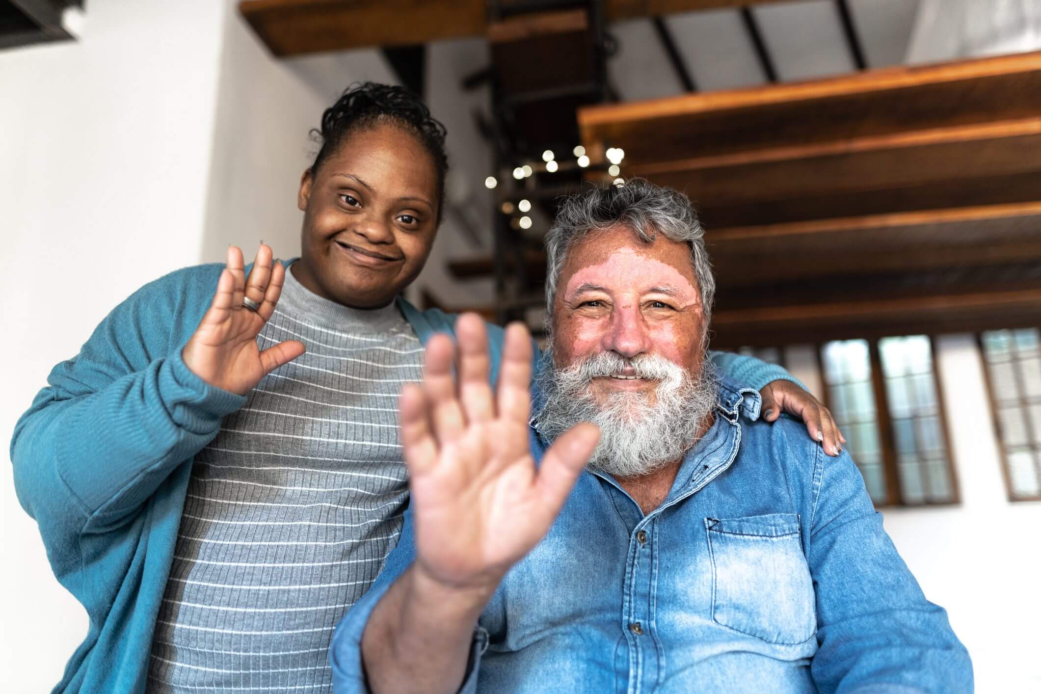 Smiling couple waving warmly at the camera indoors.