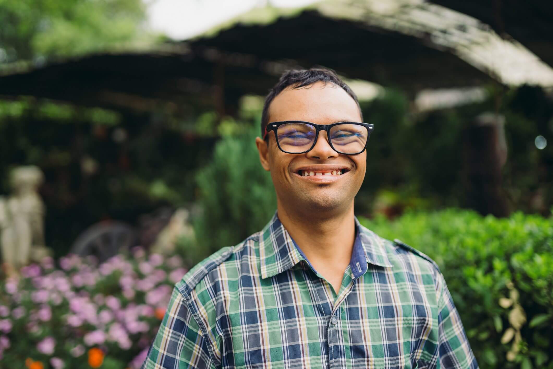 Smiling man with glasses in a green plaid shirt outdoors.